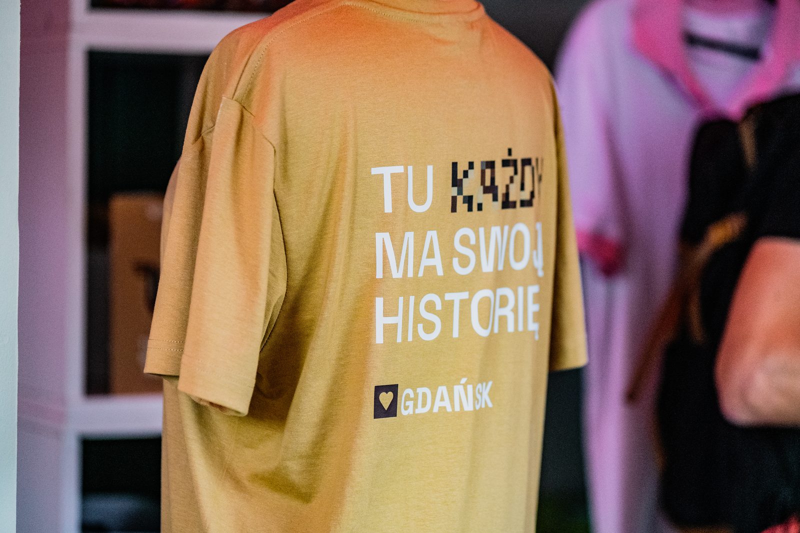 Brązowa koszulka jarmarkowa z nadrukiem „Tu każdy ma swoją historię” na plecach