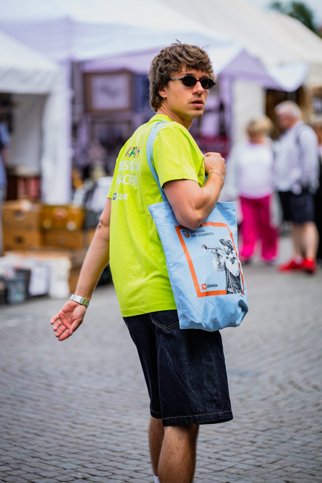 Mężczyzna w limonkowej koszulce jarmarkowej z niebieską torbą na ramieniu